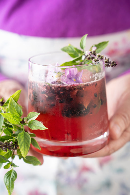 Someone holding a blackberry bourbon drink with a blackberry bramble.
