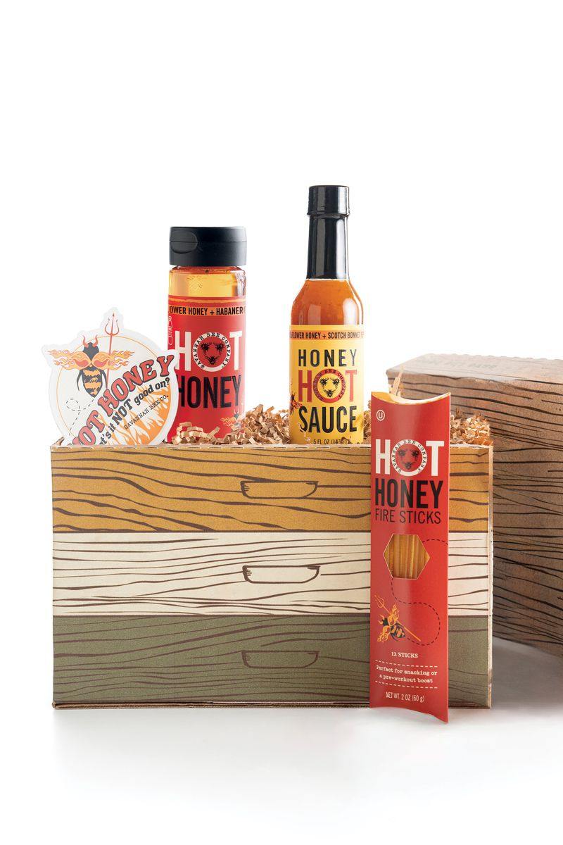Hot honey products including bottles and sticks in a wooden box on a white background